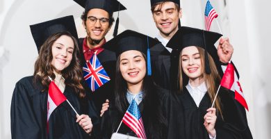 selective focus of cheerful students in graduation gowns holding flags of different countries and